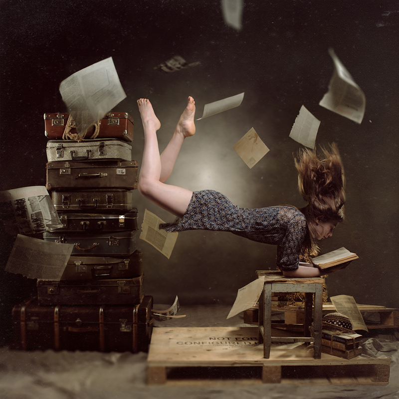 Концептуальный портрет: левитирующая девушка с книгой среди чемоданов